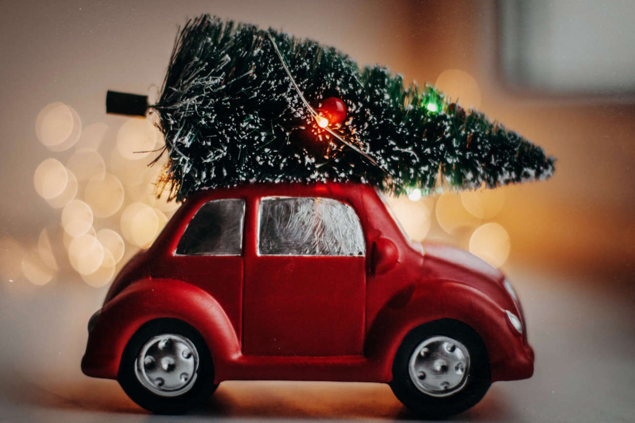 Liten lekebil som frakter et juletre på taket