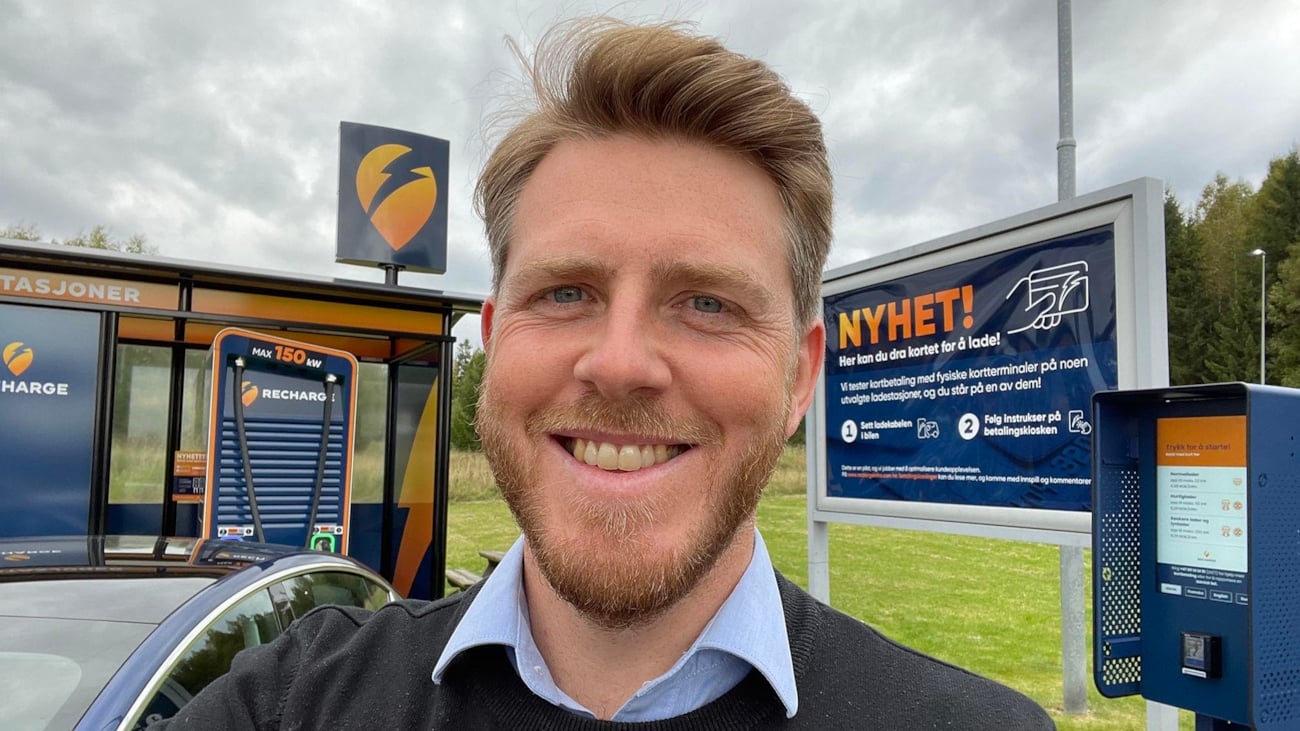 Stian Mathisen i Recharge ser mot kamera smilende med Recharge sin ladestasjon i bakgrunnen