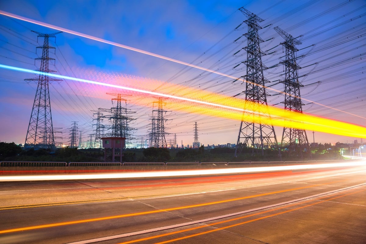 Illustrasjonsfoto hvor man ser strømmaster bak en bilvei. Bildet er tatt i skumring og med høy eksponering som gjør at billysene blir lysstriper. 